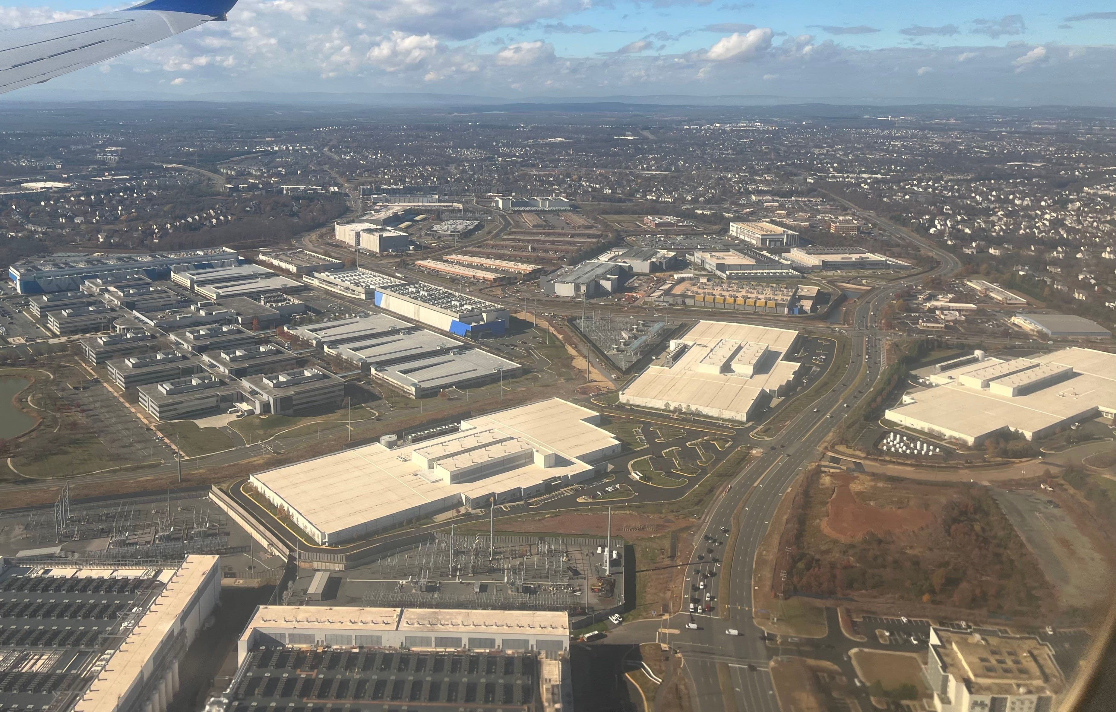 Aerial view from a plane window of large white data centre buildings, substations and roads in Ashburn, Virginia